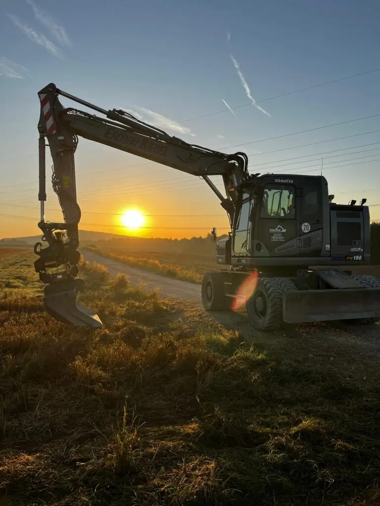 Ein Bagger der Firma Erdbau Riedel, der einen Sonnenuntergang im Hintergrund zeigt.